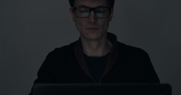 Портрет мужчины, работающего на ноутбуке поздно ночью в темной комнате — стоковое видео