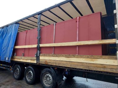 Büyük kargo konteynırlarıyla dolu bir yük kamyonu yükleme alanında park halinde. Hava bulutlu, muhtemel yağmuru gösteriyor. Kamyon teslimat için hazır..