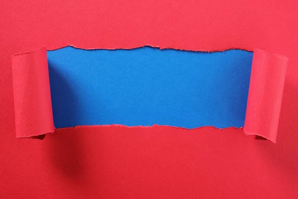 Torn red paper strip curled edge revealing center blue backgroun