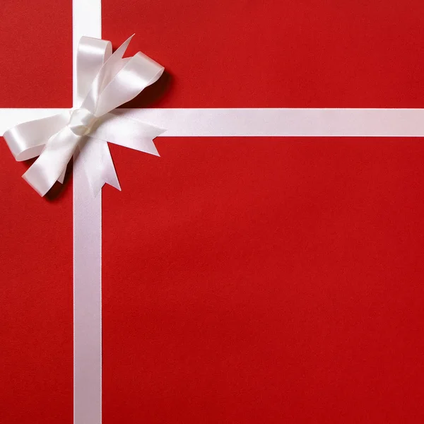 Gift wrap, white ribbon bow, red paper background, copy space — Stock Photo, Image