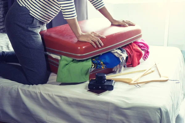girl packing the luggage prepare for her journey trip with a lot of her cloth, use her power force to close the bag by her knee