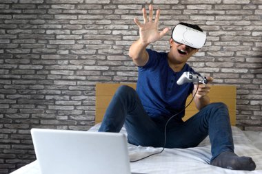 Genç adam giymek kulaklık vizyon görünümü yatak oyna comuputer veya smartphone 