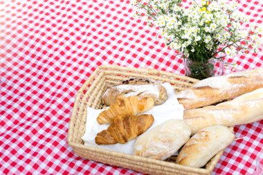 piknik ekmek kruvasan sepeti meyve portakal suyu kavanoz ile kırmızı beyaz bez ve vazo çiçek