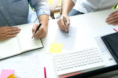 Kadın ve erkek eğitim veya iş için dizüstü bilgisayar ve kağıt işi renk kalemleriyle masada çalışırlar.