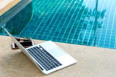 Laptop ve yüzme havuzunun yanındaki akıllı telefon, modern iş adamı her yerde çalışabilir..