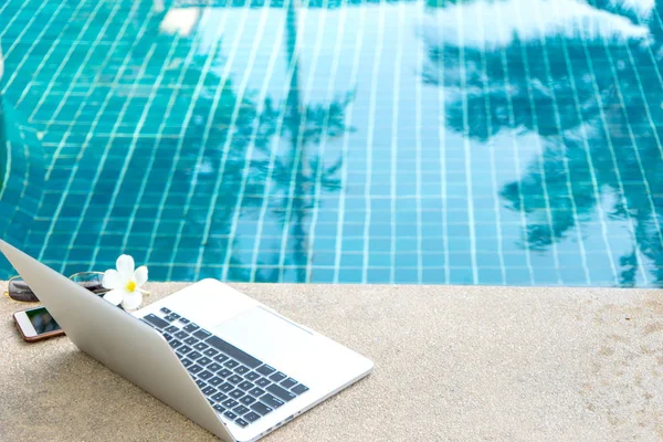 Laptop ve yüzme havuzunun yanındaki akıllı telefon, modern iş adamı her yerde çalışabilir..