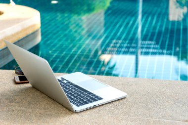 Laptop ve yüzme havuzunun yanındaki akıllı telefon, modern iş adamı her yerde çalışabilir..