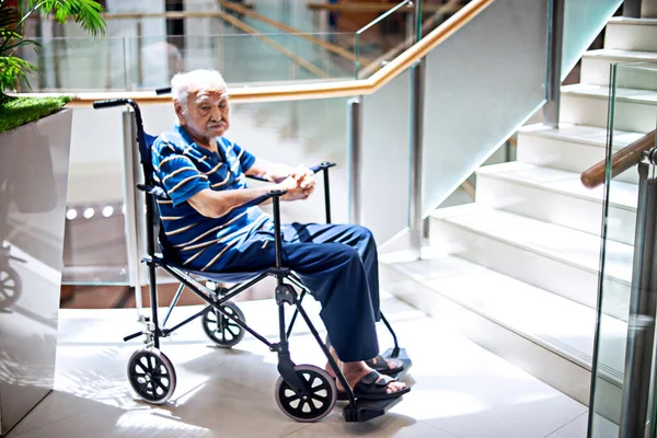 Ο γέρος κάθεται σε αναπηρική καρέκλα και γεμίζει μοναξιά στο εμπορικό κέντρο. — Φωτογραφία Αρχείου