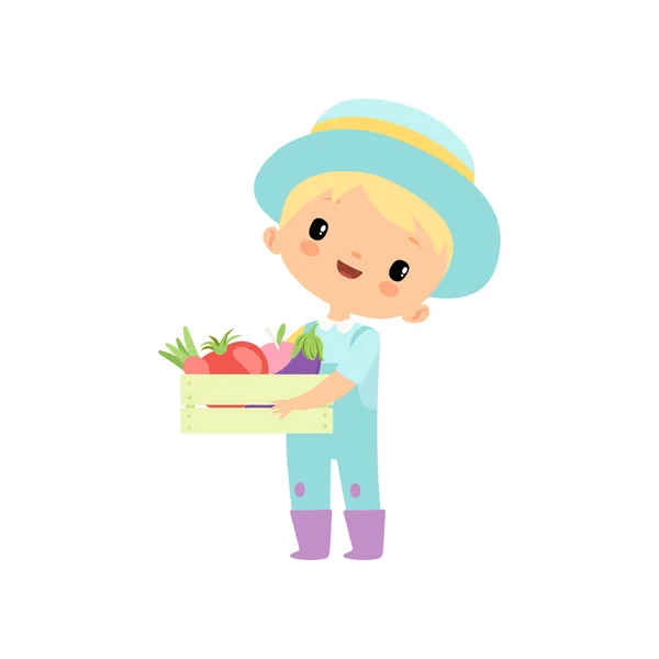 Lindo niño en overoles, botas de goma y sombrero sosteniendo caja de madera llena de verduras, personaje de dibujos animados de agricultores jóvenes comprometidos en actividades agrícolas Vector Ilustración — Vector de stock