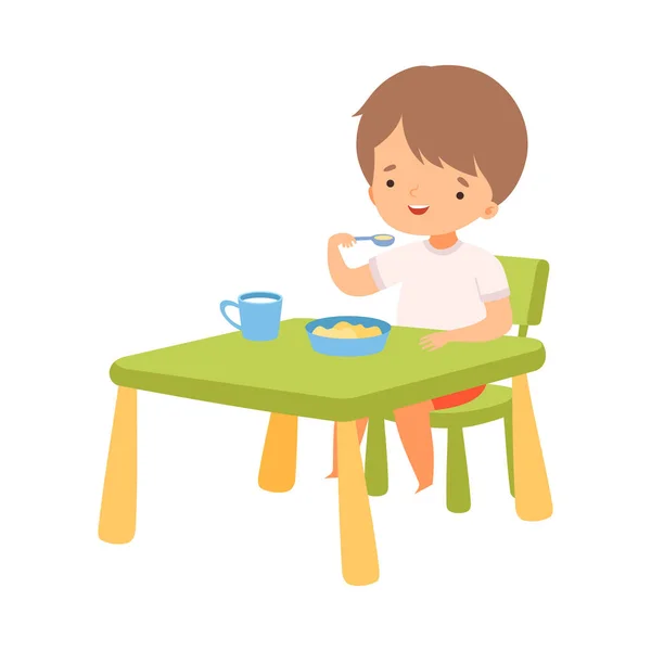 かわいい男の子がテーブルで朝食を食べる、就学前の子供の毎日のルーチン活動漫画ベクトルイラスト — ストックベクタ
