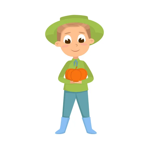 Симпатичный мальчик, держащий в руках спелую тыкву, персонаж маленького фермера в зеленом цвете, работающий в стиле садовых мультфильмов — стоковый вектор