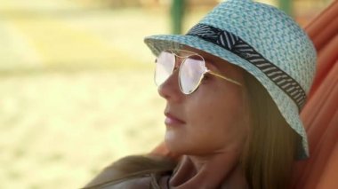 Sahildeki hamakta gözlüklü ve şapkalı bir kız.