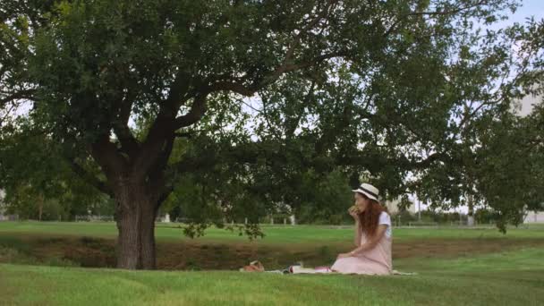 Mooie vrouw eet verse appel zittend in de zomertuin — Stockvideo
