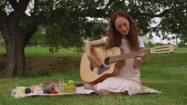 Piękna dziewczyna gra na gitarze akustycznej w parku. — Wideo stockowe