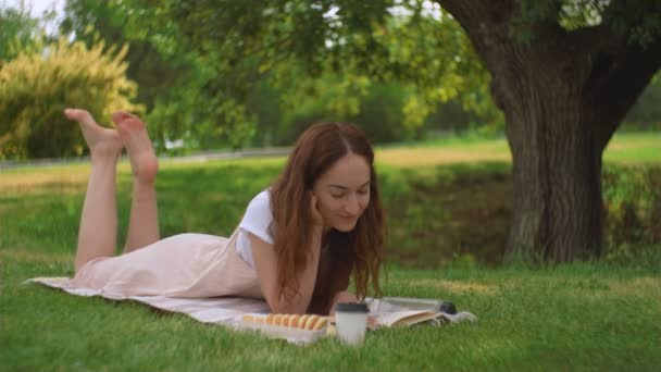 Mladá žena lže a čte knihu v parku — Stock video