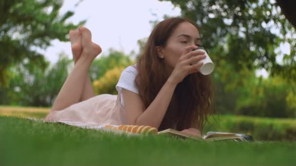 Giovane bella donna che beve caffè su un'erba in un parco estivo . — Video Stock