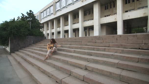 Mulher tocando guitarra acústica nas escadas perto da universidade — Vídeo de Stock