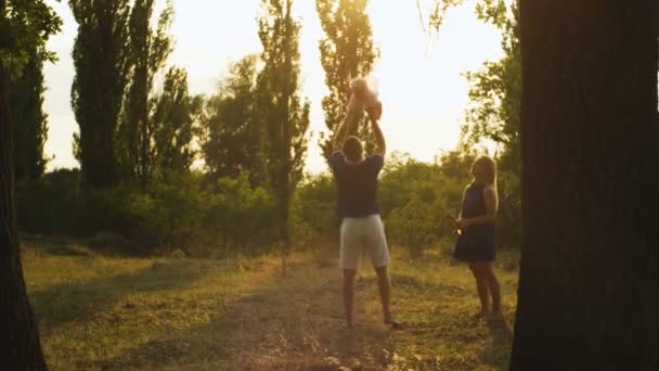 Счастливый отец бросает своего ребенка в парке против заката — стоковое видео