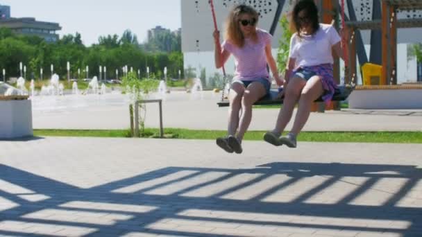 Slide shot van Happy twee meisjes rijden op een schommel in de zomer park. — Stockvideo