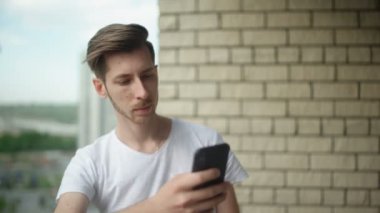 Beyaz tişörtlü genç adam akıllı telefonunu kullanarak internette geziniyor.