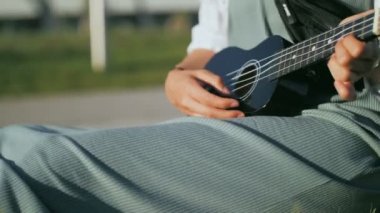 Genç bir kadın ukulele çalıyor, izin günlerinde gitar çalıyor.