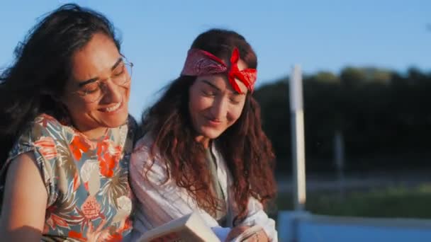 Gadis cantik siswa modern mengalami percakapan di taman berbicara dan tertawa memegang buku dan kopi — Stok Video