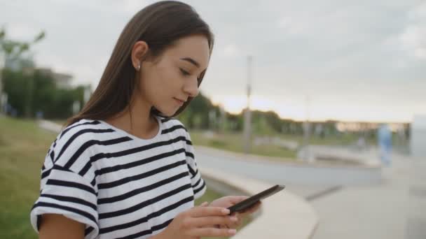 Retrato de menina atraente sentado no banco lendo um livro ao ar livre — Vídeo de Stock