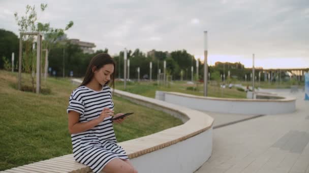 Mooie jonge vrouw leest een boek op de bank buiten bij zonsondergang — Stockvideo