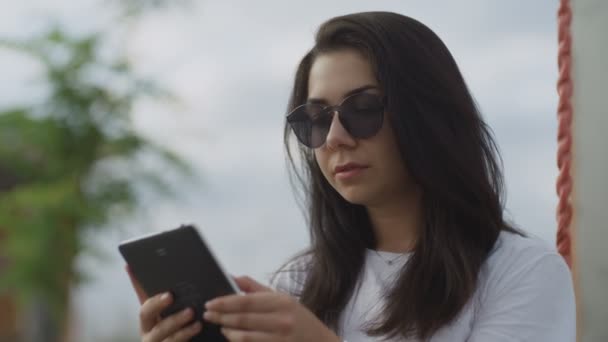 Vacker kvinna i solglasögon läser ebook utomhus — Stockvideo