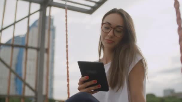 Красивая женщина в очках читает электронную книгу в парке — стоковое видео