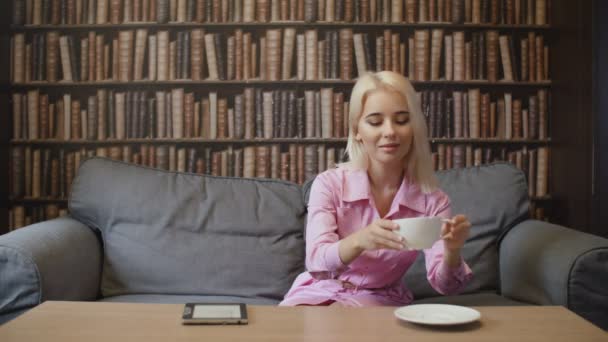 金髪の女がコーヒーを飲み、カフェで本を読む — ストック動画
