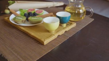 Yeşil çayla demlik, iki fincan ve meyve.