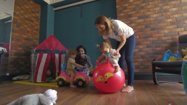 Moms with childs playing. Girl jumping on a red ball — Stock Video