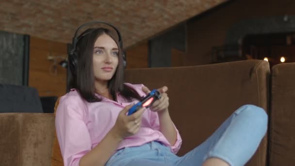 拿着耳机的女人坐在沙发上玩电子游戏 — 图库视频影像