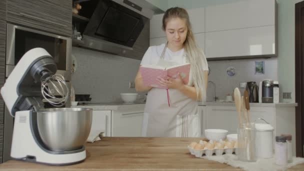 Ama de casa leyendo receta en libro de cocina en la cocina — Vídeo de stock