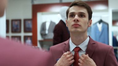 Adam aynaya bakıyor ve butikte kırmızı bir ceket giyiyor.