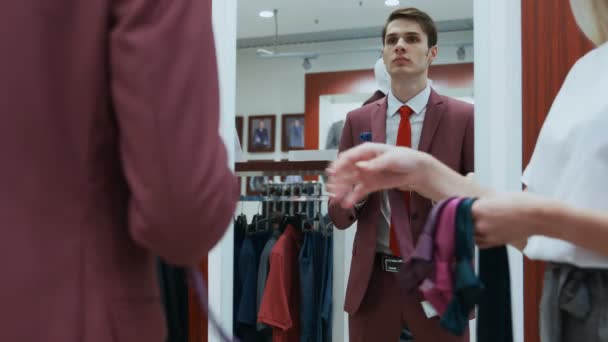 Hombre vestido con elegante traje rojo mira al espejo y elige su corbata — Vídeo de stock