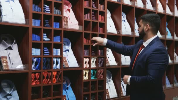 Бизнесмен в синей куртке выбирает галстук в магазине — стоковое видео