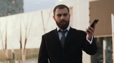 Takım elbiseli iş adamı modern bina arka planında cep telefonuyla konuşuyor..