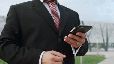 Klasik takım elbiseli bir iş adamı açık havada akıllı telefon kullanıyor.