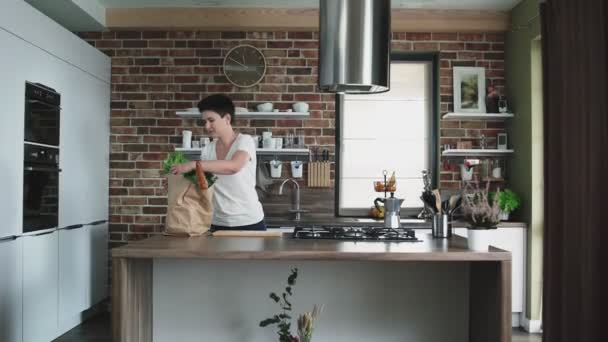 Glad ung kvinna tar till köket en stor papperspåse med matvaror. — Stockvideo