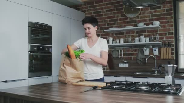 Mulher sorridente na cozinha com um saco de compras — Vídeo de Stock