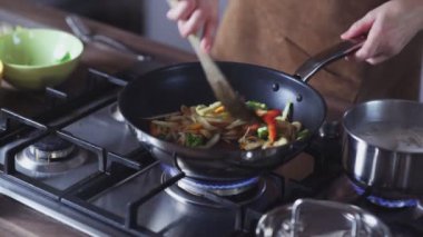 Evde tavada sebze kızartan bir kadın.