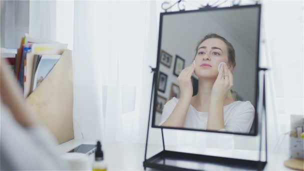 Belle femme de nettoyage visage avec des tampons de coton devant le miroir — Video