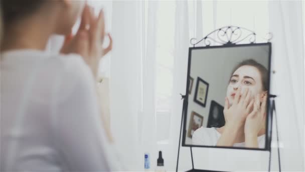 Γυναίκα βάζει μάσκα προσώπου στο πρόσωπό της μπροστά στον καθρέφτη — Αρχείο Βίντεο