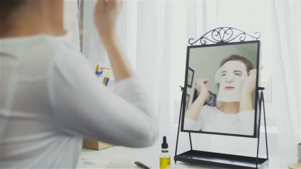Žena použití kosmetických japonskou masku na tváři a při pohledu do zrcadla — Stock video