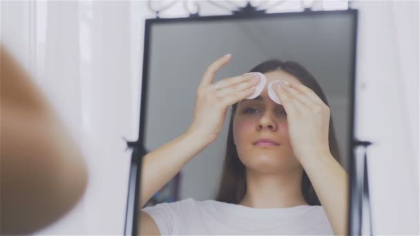 Mujer joven limpiando la cara con almohadillas de algodón en frente del espejo — Vídeo de stock