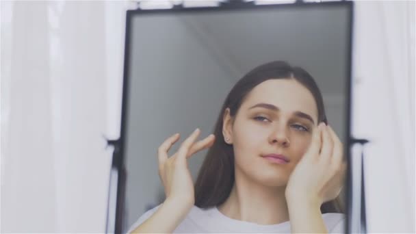 El retrato de una mujer joven con la piel perfecta aplicando una crema de día y noche en su cara . — Vídeos de Stock