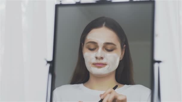 Женщина надевает маску на лицо перед зеркалом — стоковое видео
