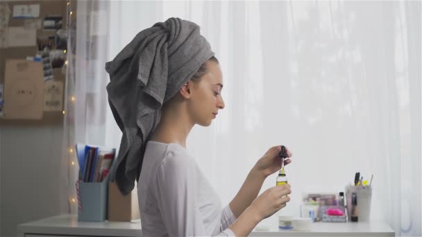 Wanita dengan handuk di kepala mengoleskan minyak lotion di wajahnya — Stok Video